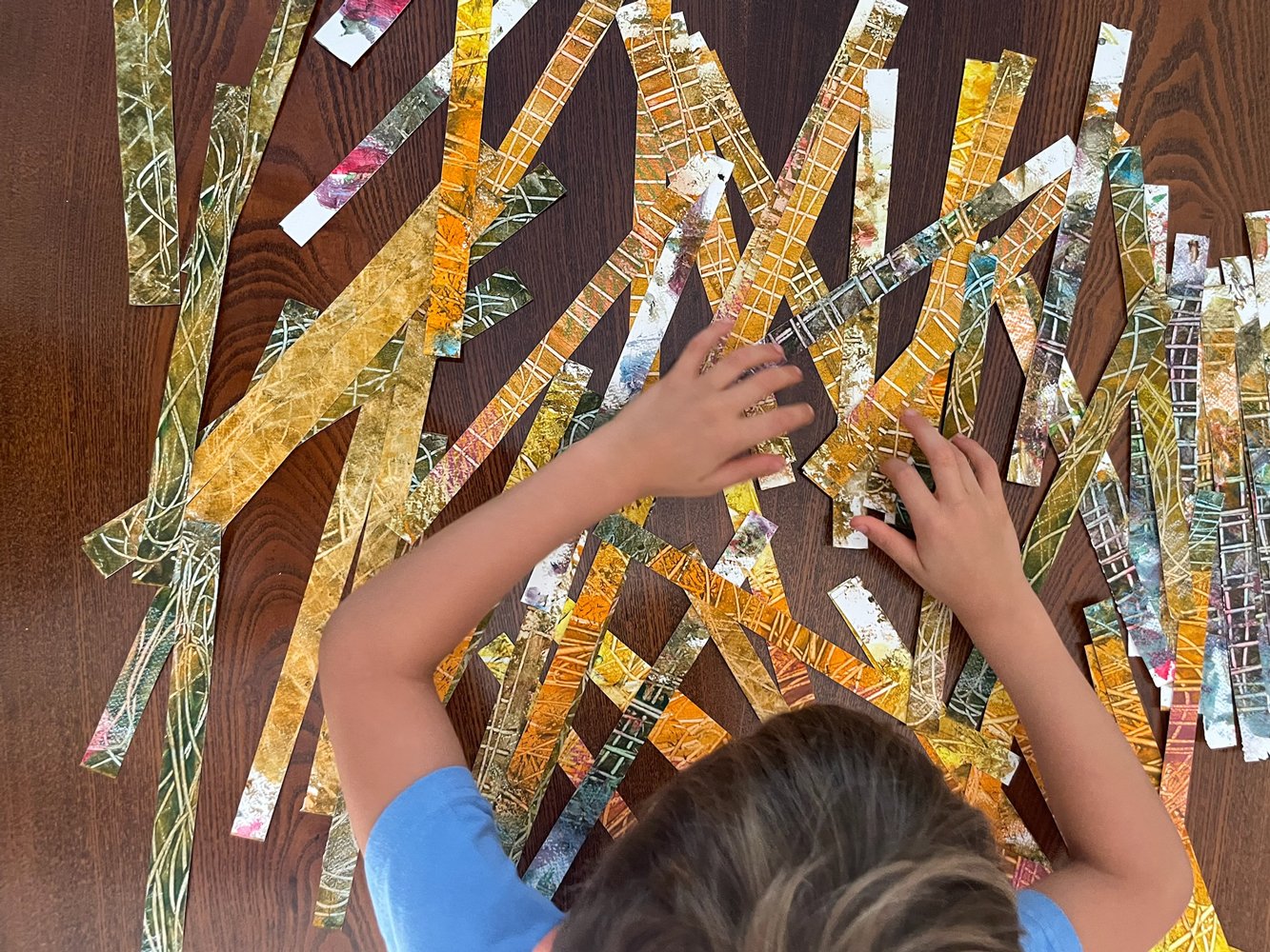 Child arranging colorful paper strips with nature scenes on a wooden table.