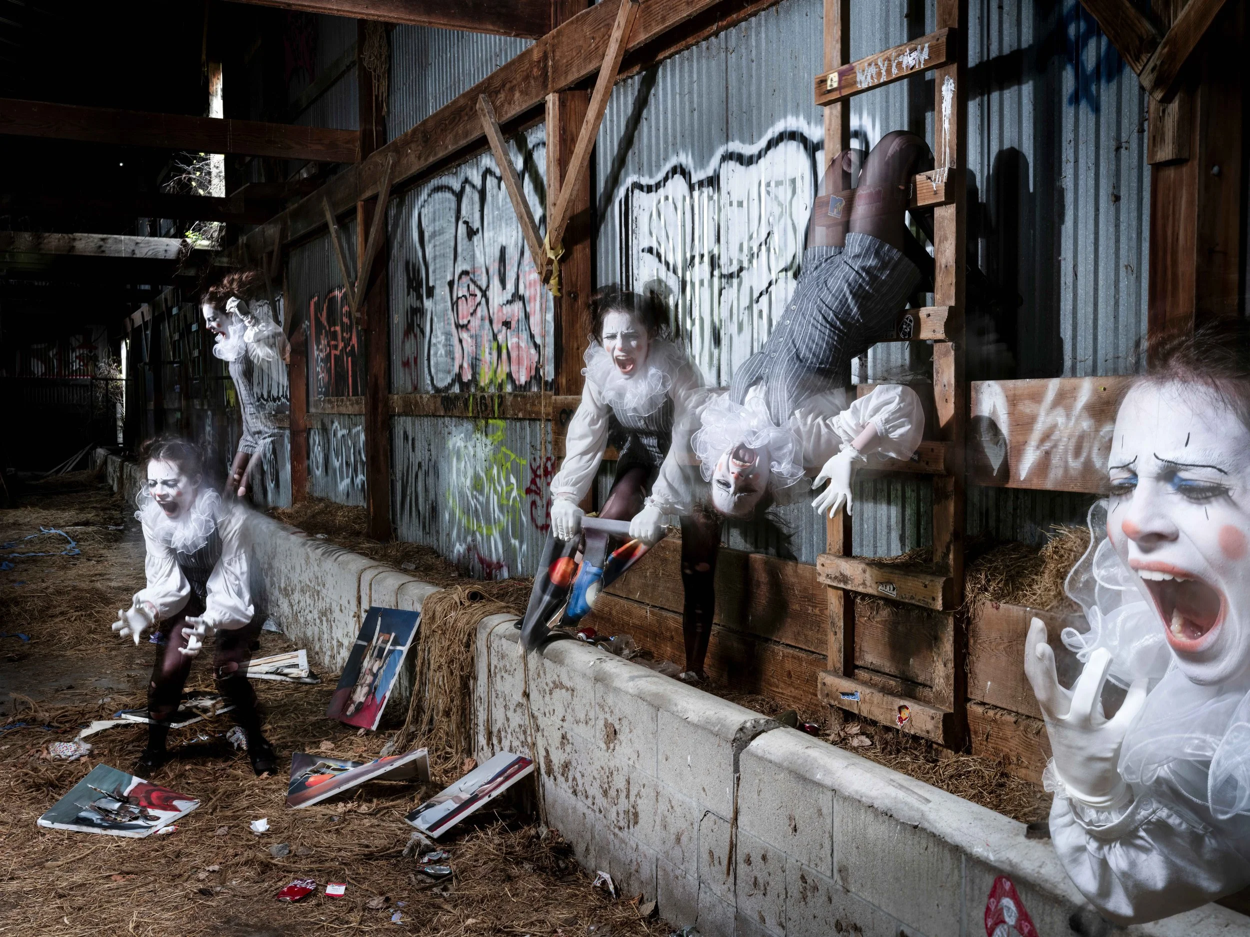 Clowns with white face paint and costumes, disturbing expressions, in an abandoned area with graffiti, wooden structures, and scattered magazines.