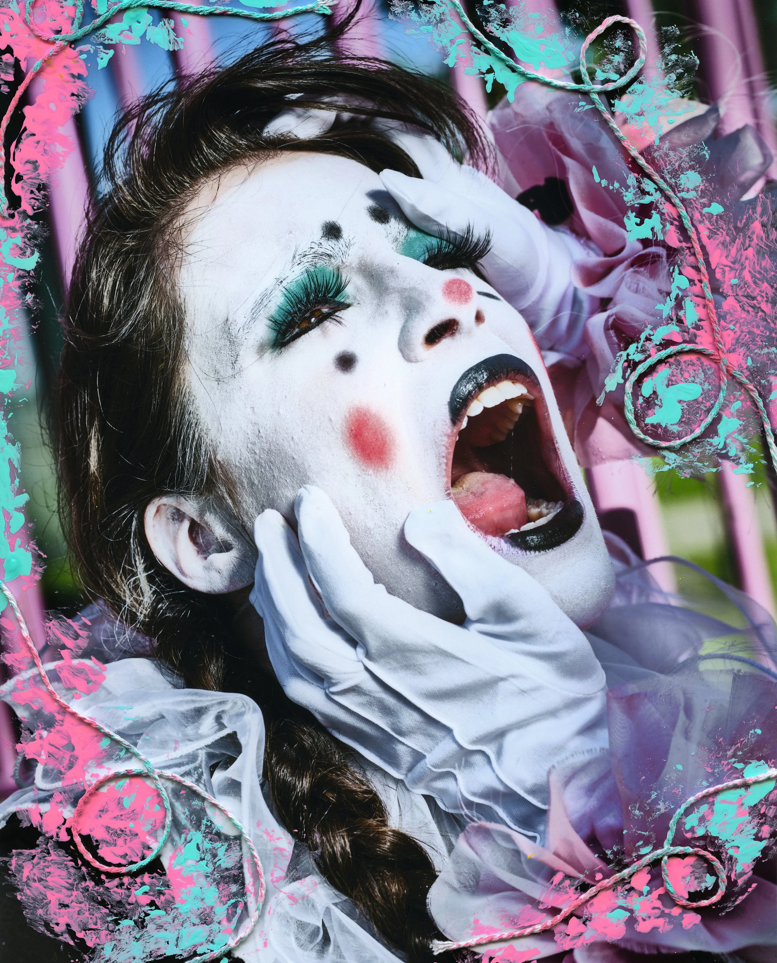 A person lying with eyes closed, face painted white with black dots and red cheeks, colorful makeup, and long dark hair. They wear white gloves and a pastel pink jacket, surrounded by pink and teal decorative elements and splatters.