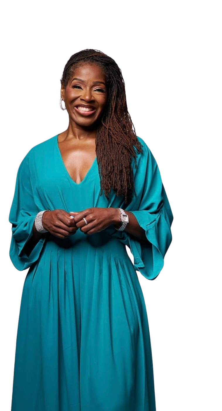A smiling woman with long dreadlocks wearing a teal dress, jewelry, and standing against a black background.