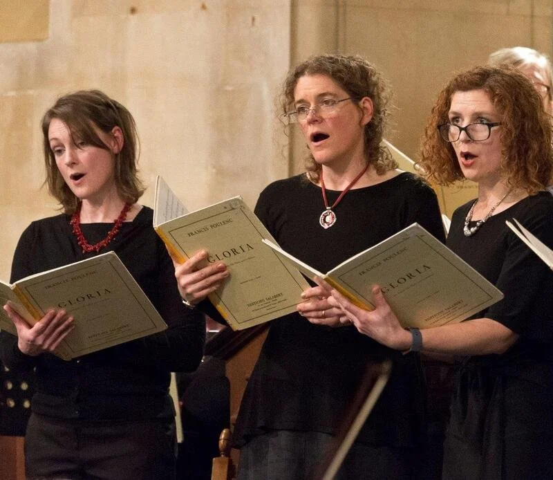 Three women singing in a choir, holding music books.