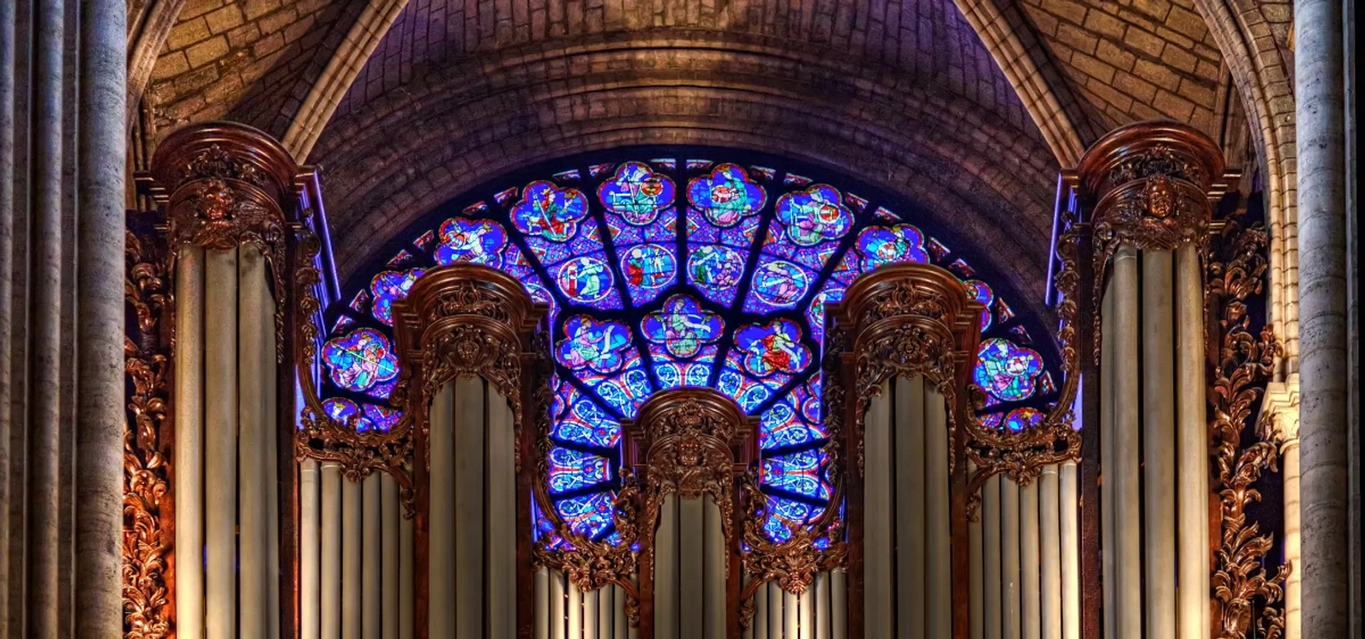 Colorful stained glass window above ornate wooden organ pipes inside a cathedral