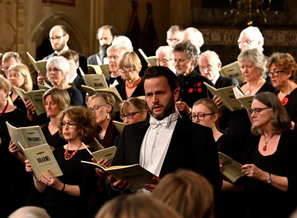 A choir performing in a church, with many people holding open songbooks, including a young man in the foreground wearing a tuxedo.