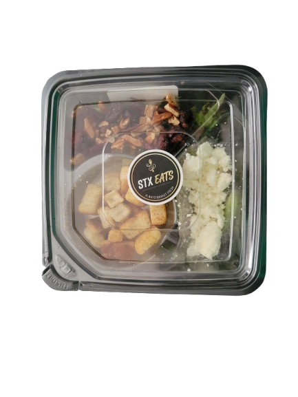 A clear plastic takeout container with a black sticker labeled 'STX Eats' on the lid, containing chopped vegetables, roasted meat, and potato flakes.