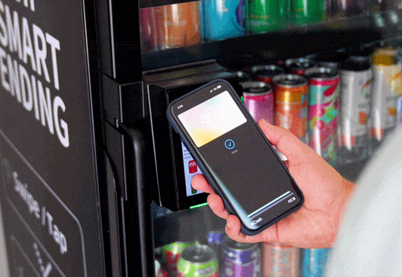 Person using a smartphone to pay with digital wallet at a vending machine filled with canned drinks.