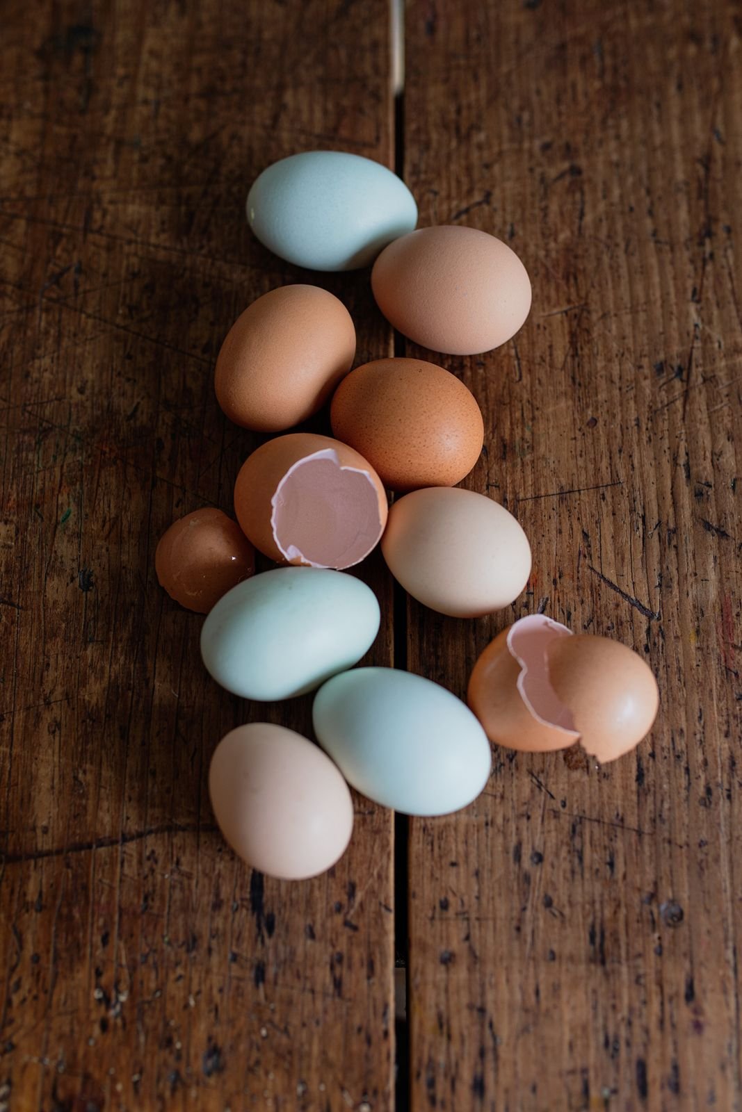 Colorful eggs, some broken open, arranged on a wooden surface.