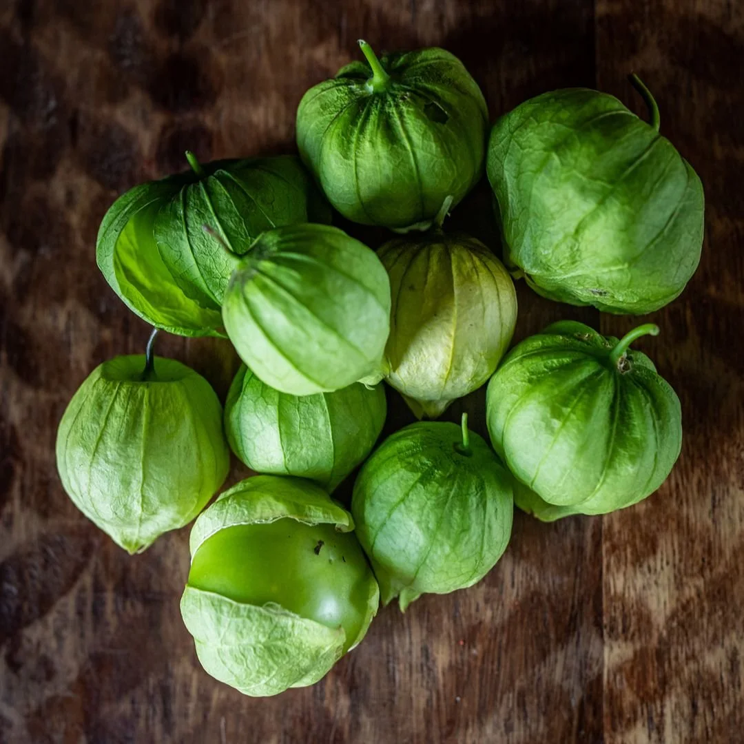 A bunch of fresh green tomatillos with leafy tops on a wooden surface.