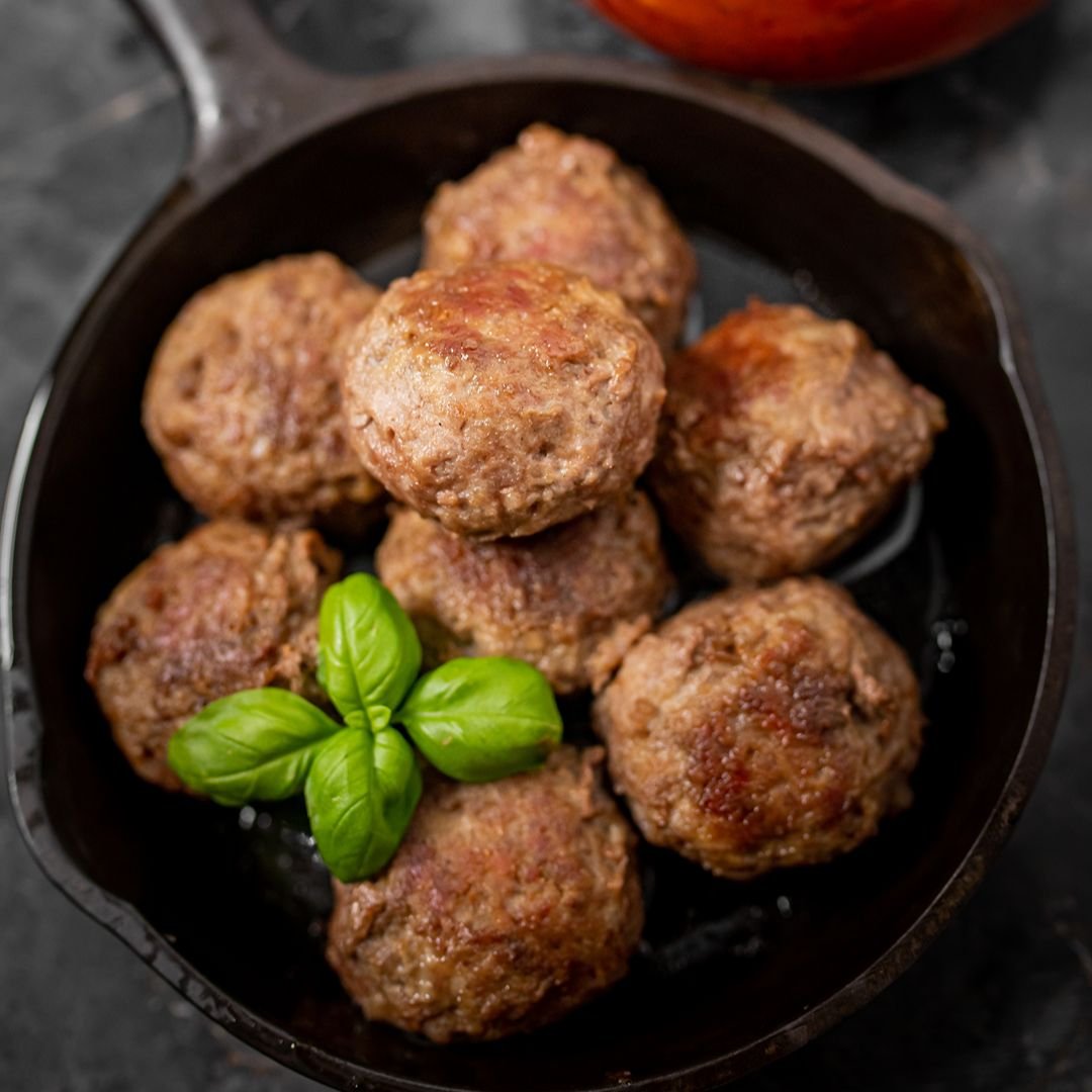 Several cooked meatballs garnished with fresh basil leaves served in a black skillet.