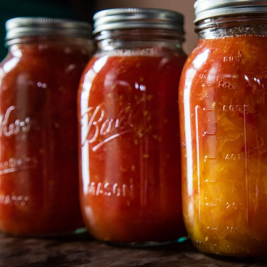 Three glass jars filled with homemade fruit preserves or jam on a wooden surface.