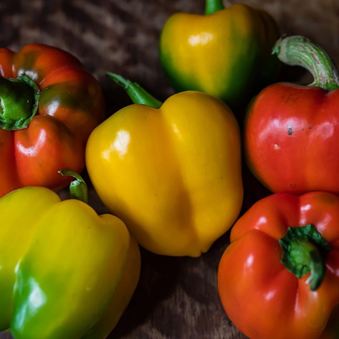 A close-up of colorful bell peppers on a wooden surface, including yellow, red, orange, and green peppers.