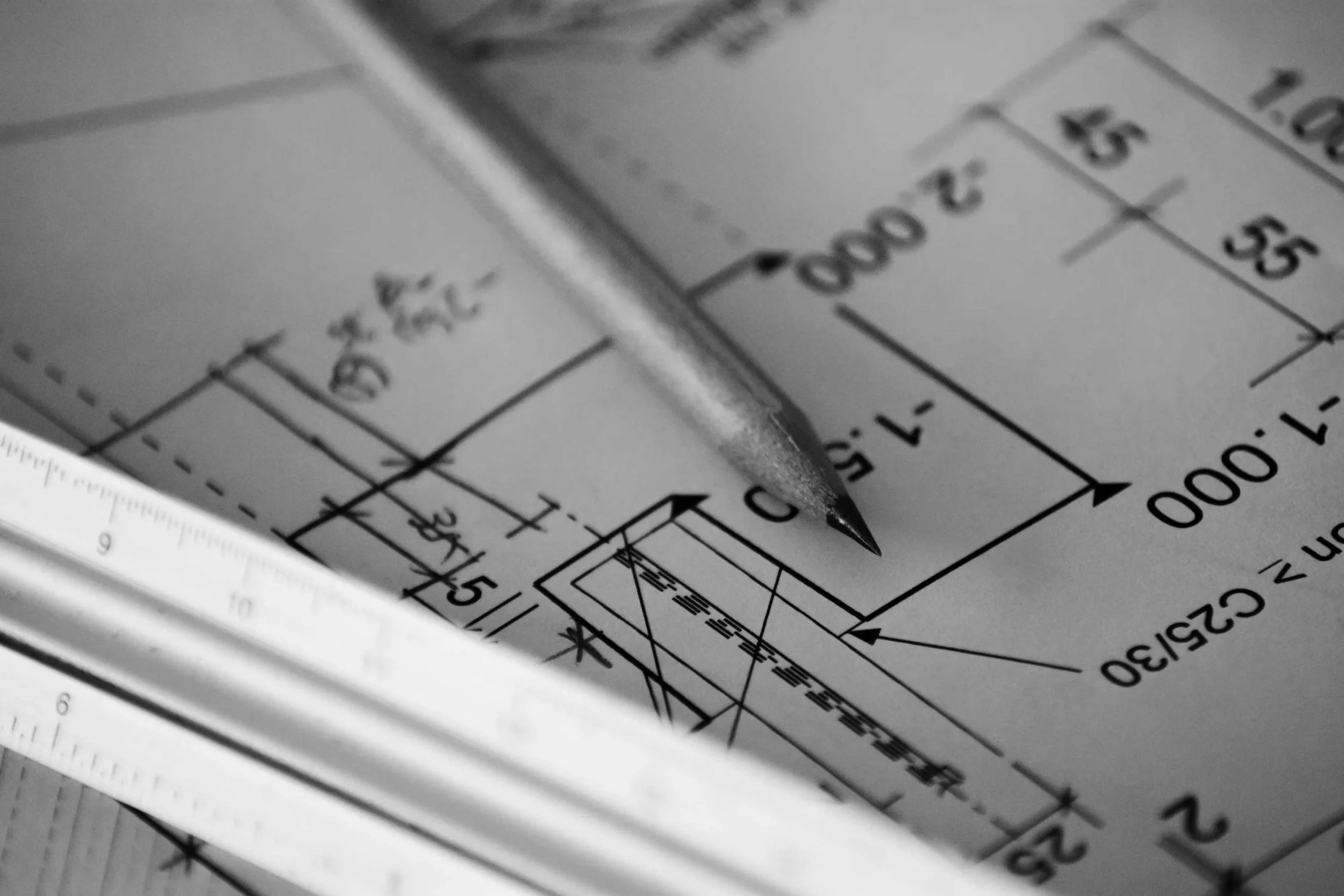 Close-up of technical drawings or blueprints with measurements and diagrams, featuring a metallic tool or caliper placed on top.