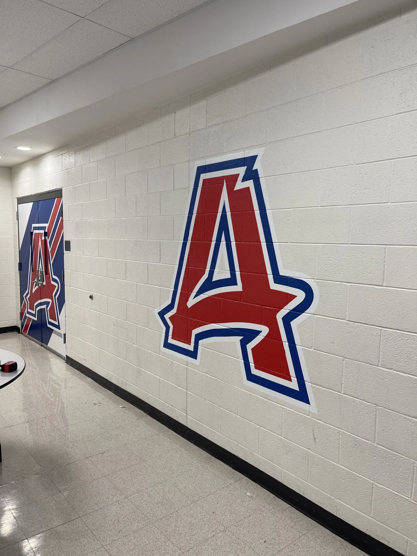Hallway wall with large logo of the Los Angeles Angels baseball team painted on it, with a door to the left.