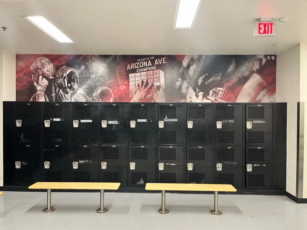 School lockers and benches in a hallway with a sports-themed mural on the wall.