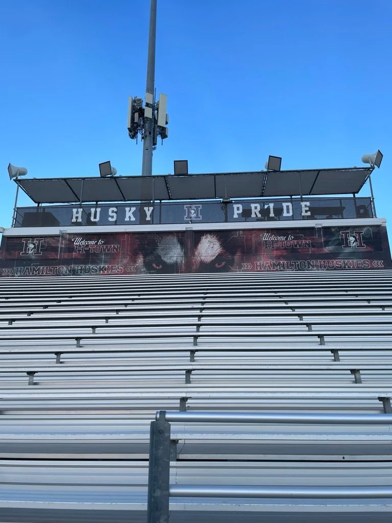 View of a sports stadium seating area with a banner that reads "Husky Pride" and displays a fierce husky dog with glowing eyes, under a clear blue sky.