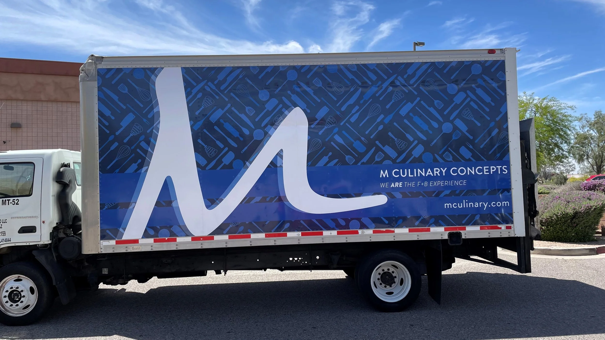 A truck with a blue and white advertisement for M Culinary Concepts, featuring kitchen utensils in the background and the company's website, mculinary.com.