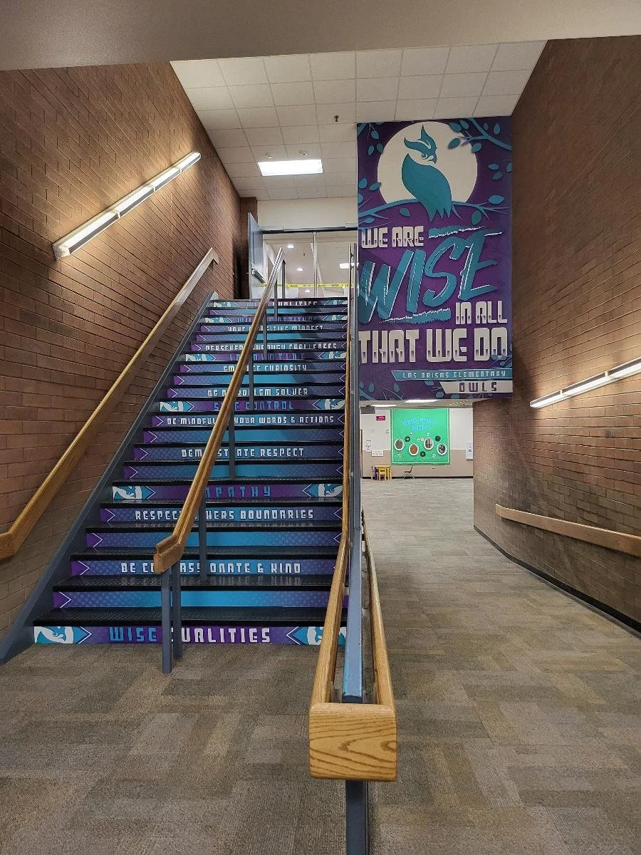 School staircase with inspirational writing on the steps and a large banner on the wall that says, "We are wise in all that we do," with an owl graphic and the name Las Brisas Elementary.