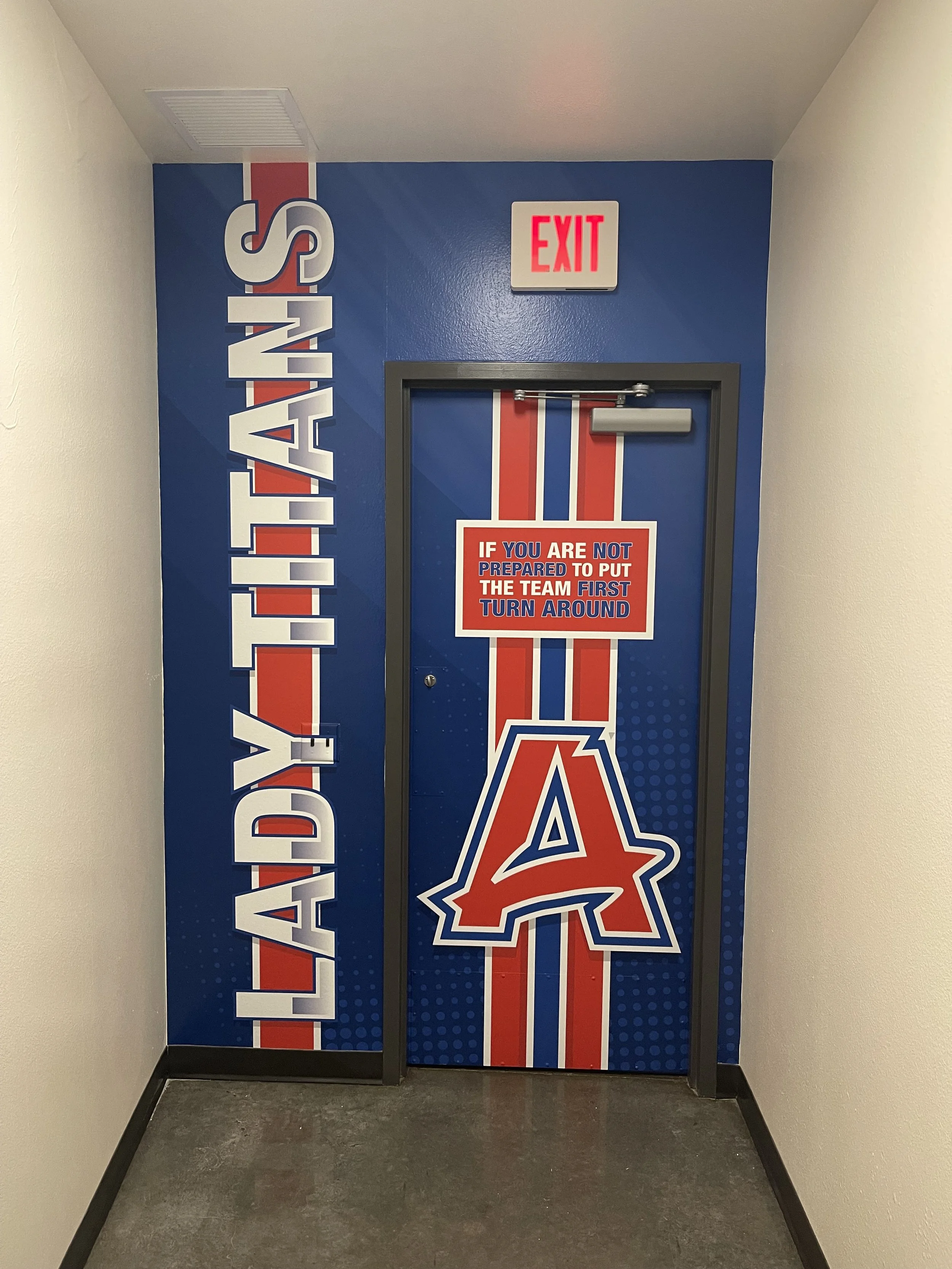 A door decorated with a similar red, white, and blue design, featuring the Los Angeles Angels logo and a sign that says, "If you are not prepared to put the team first, turn around." There is also a sign above the door that says, "EXIT."