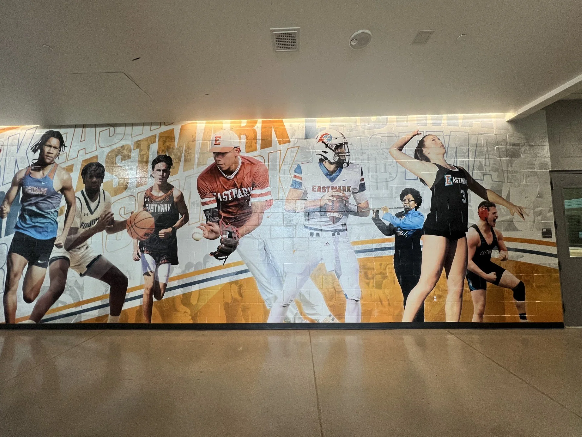 A large poster of diverse athletes, including runners and football players, on a brick wall, promoting Eastmark sports teams.