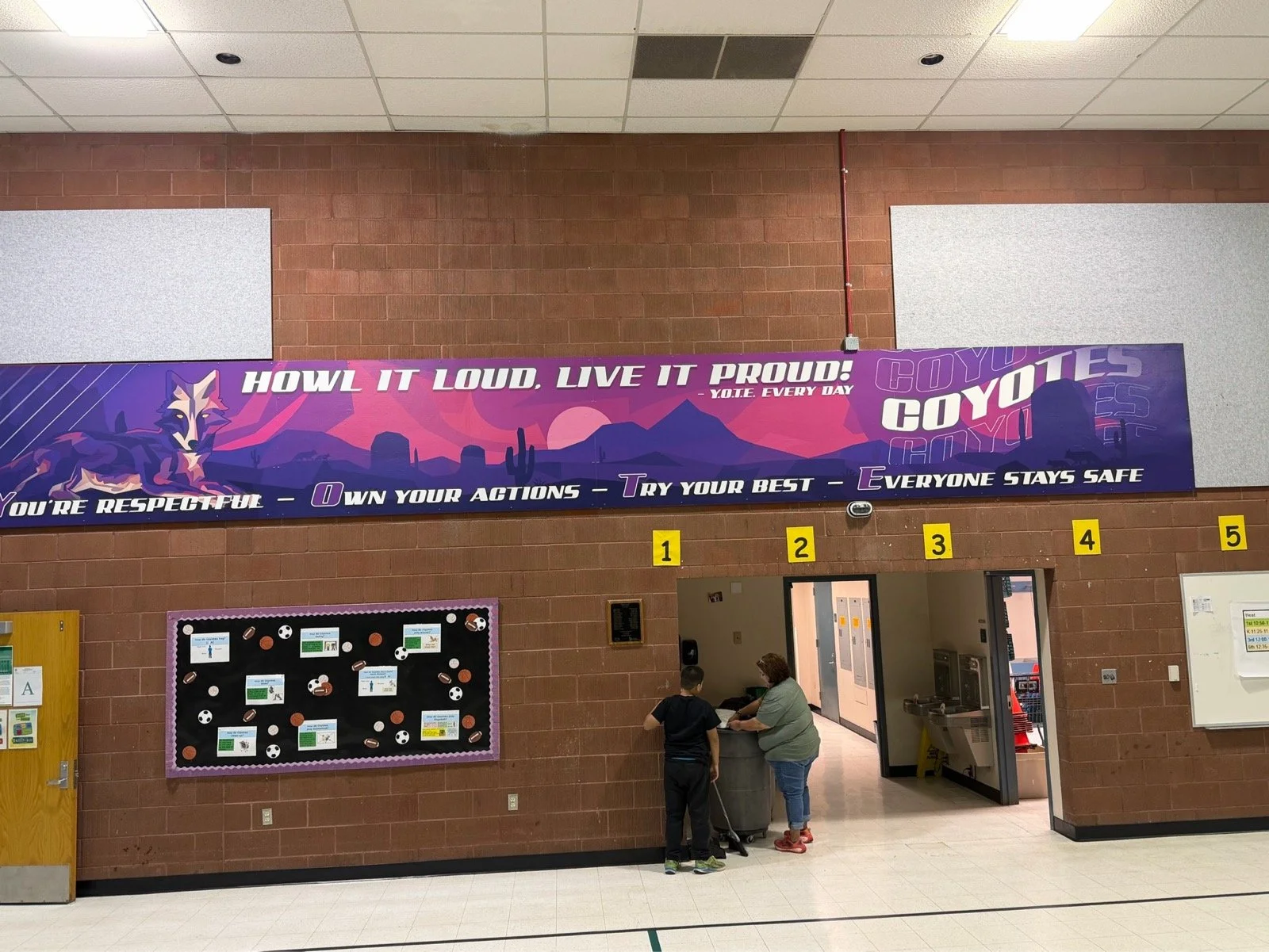 A motivational banner on a school brick wall reading 'Howl it loud, live it proud! - Y.O.T.E. every day' with a wolf graphic and desert landscape background. Below, a quote states, 'You're respectful - Own your actions - Try your best - Everyone stay