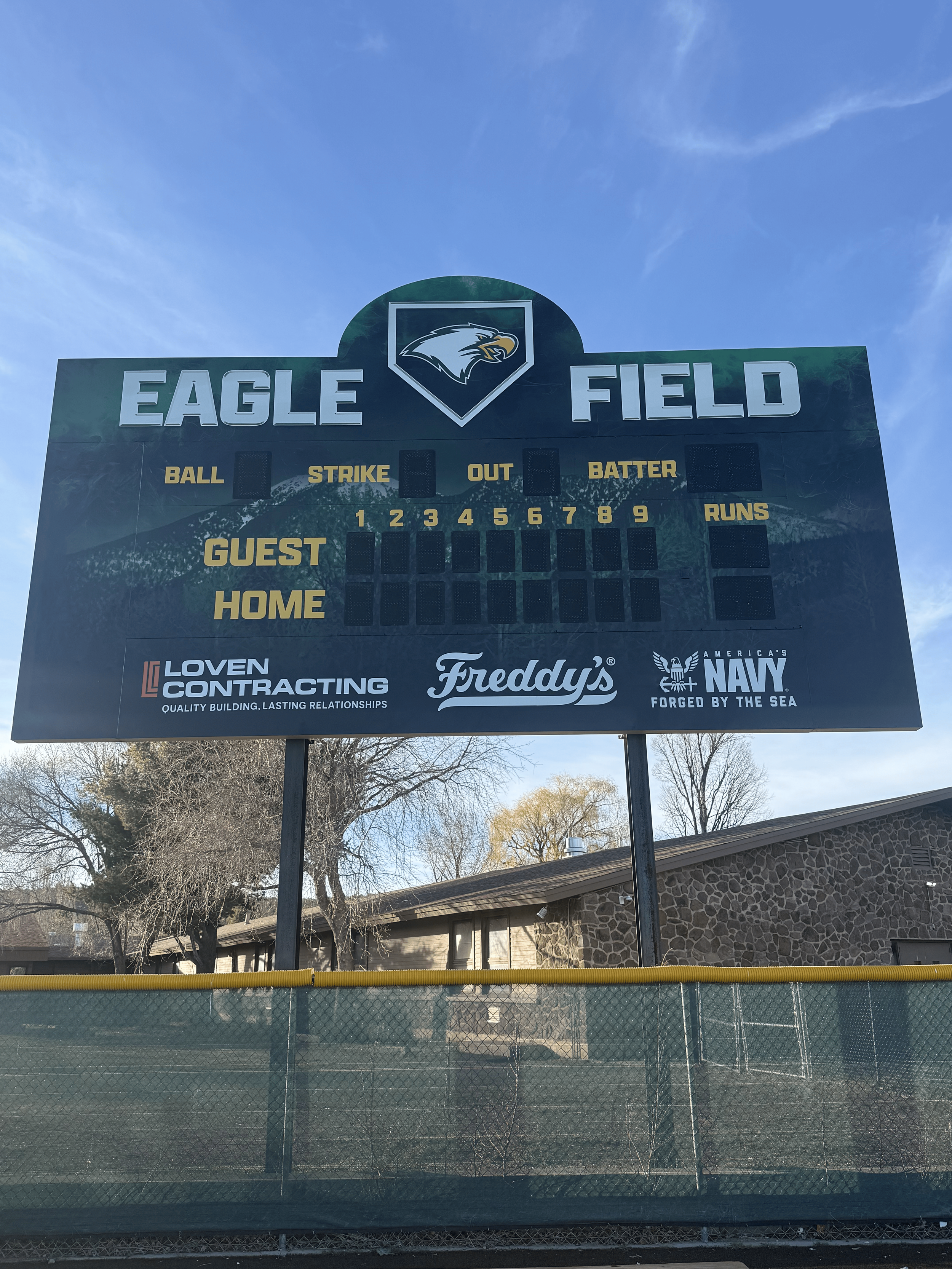 A scoreboard at Eagle Field with the Eagle logo at the top center, displaying labels for balls, strikes, outs, and runs, as well as spaces for guest and home team scores, with some corporate logos at the bottom.
