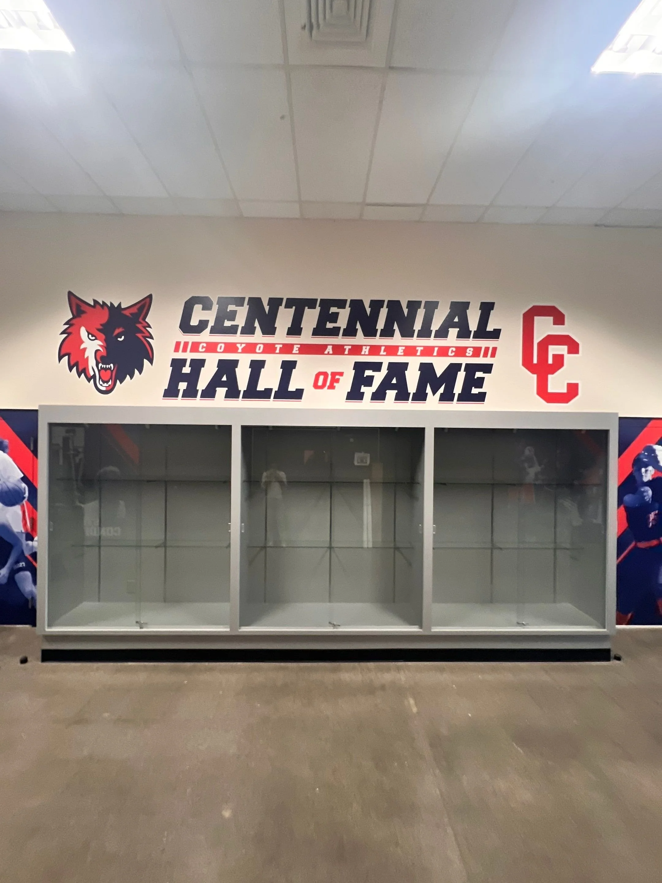 Empty display case in a sports arena with a wall graphic reading 'Centennial Hall of Fame' and the logo of Coyotes Athletics.