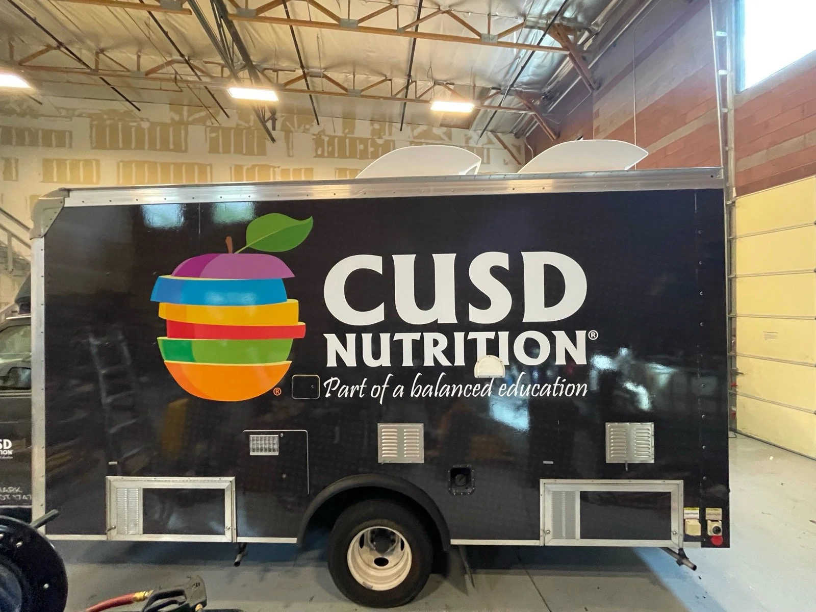 A black CUSD Nutrition food trailer with a colorful apple logo and the slogan "Part of a balanced education."