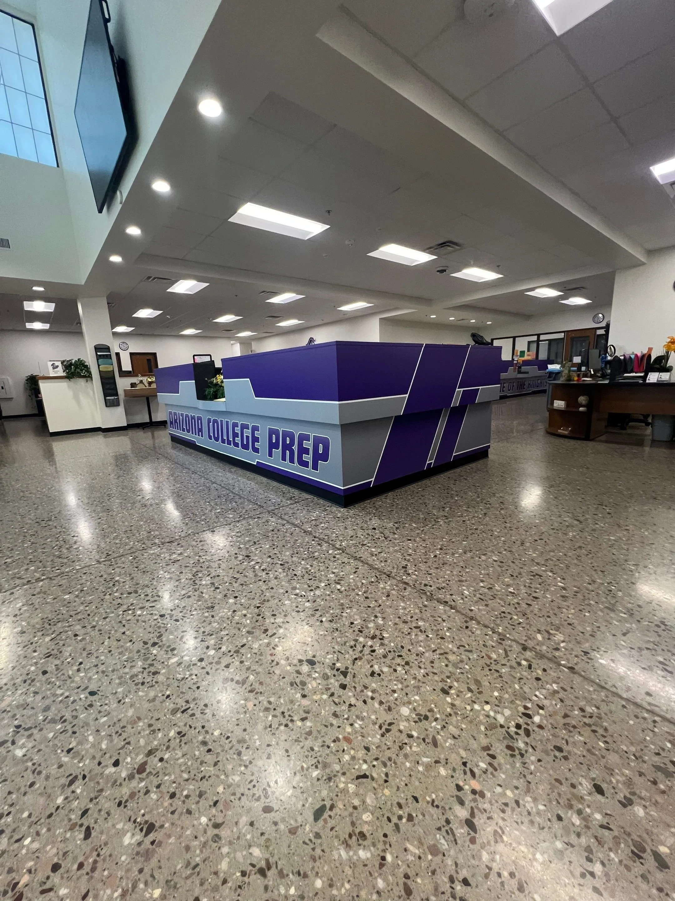 Interior of Arizona College Prep with a purple reception desk, tiled floor, and ceiling lights.