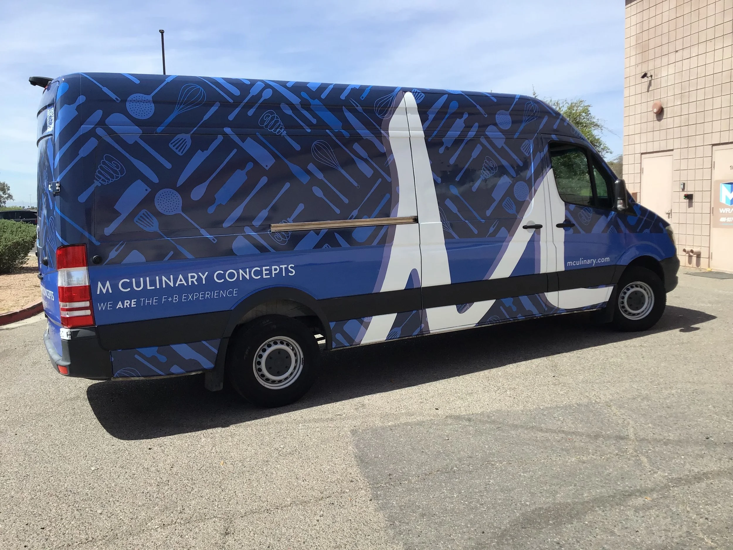 A delivery van with a blue and black design featuring kitchen utensils, and the words 'M Culinary Concepts' on the side.