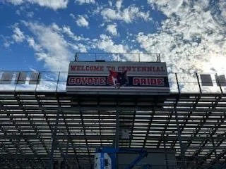 Football stadium with a digital scoreboard displaying 'WELCOME TO UNIVERSITY COWBOY PRIDE' against a sky with clouds.