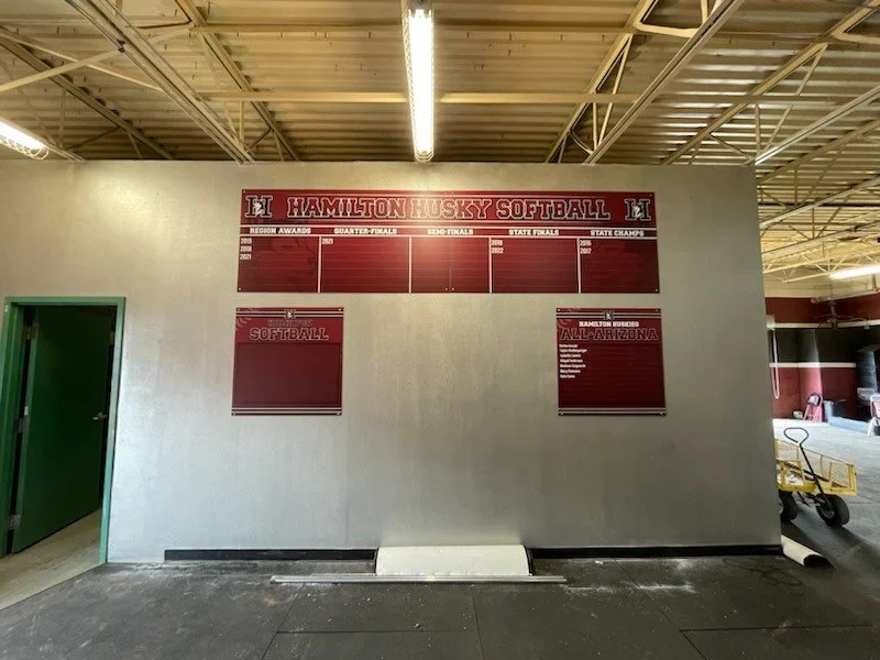 Wall display at Hamilton Husky Softball with sections for regional awards, quarter-finals, semi-finals, state finals, and state champions; two smaller posters for softball and all-Arizona team.