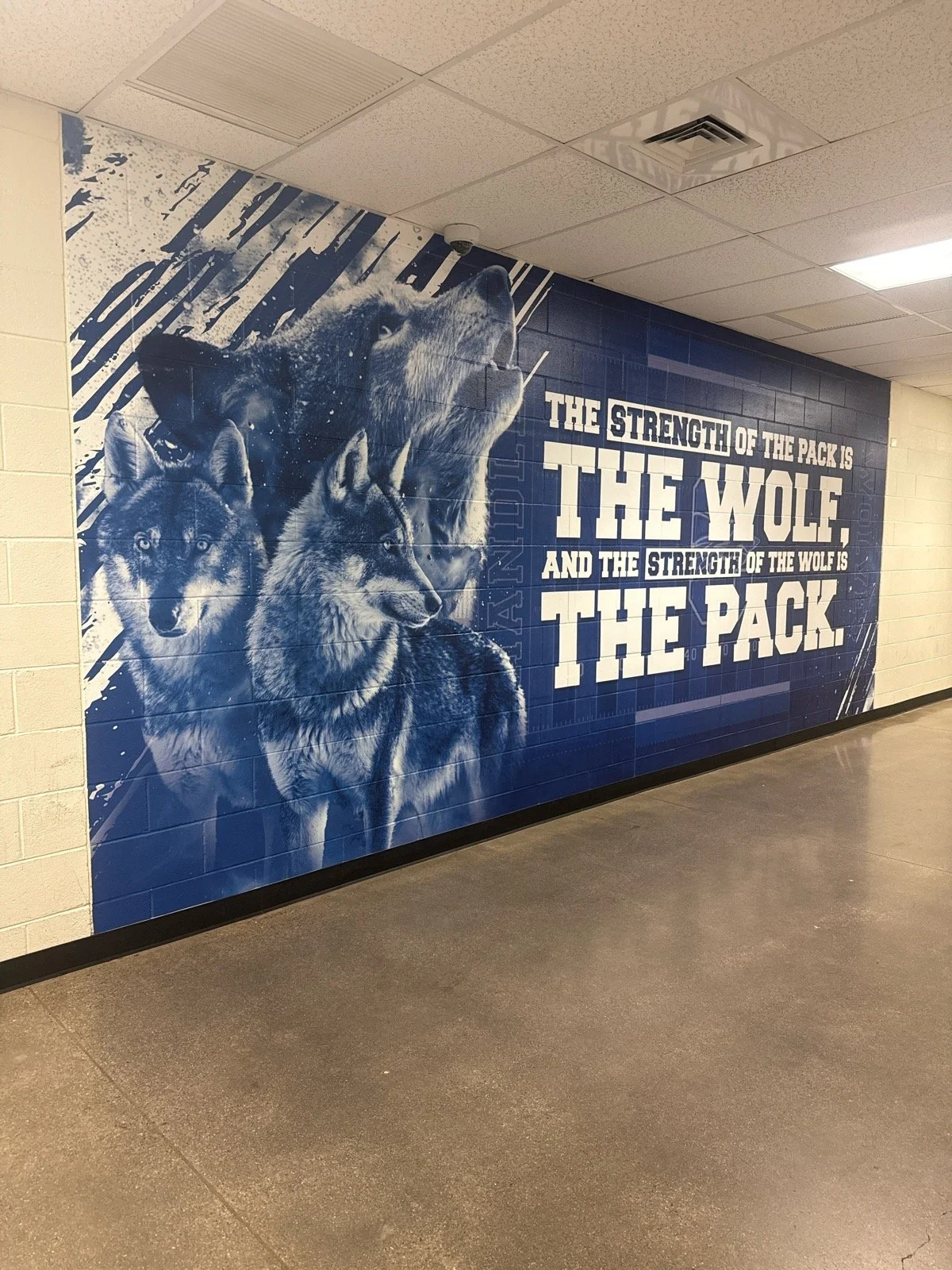 A blue and white mural in a school hallway featuring images of three wolves and the quote, "The strength of the pack is the wolf, and the strength of the wolf is the pack."