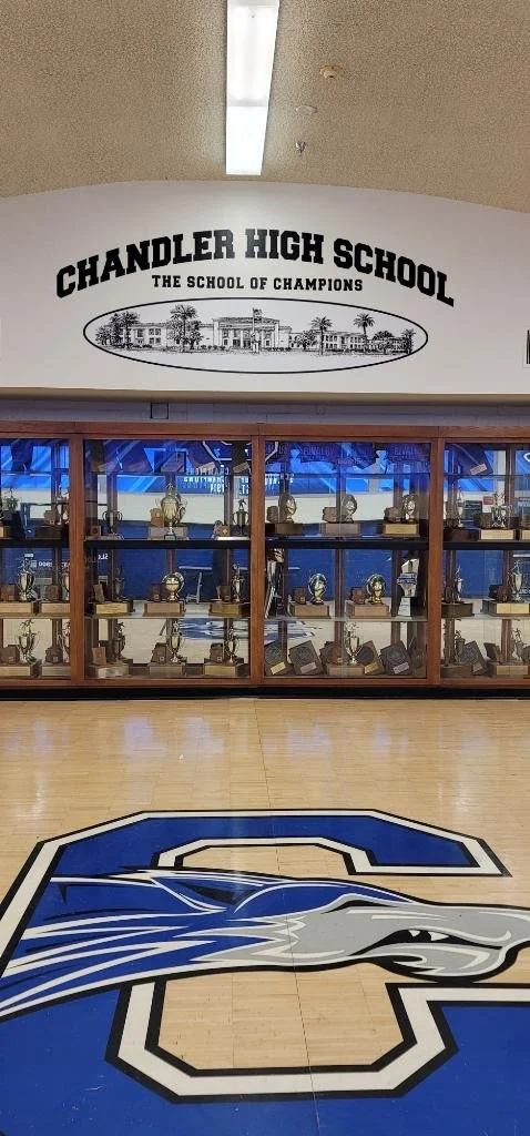 Chandler High School gym with school logo on the floor and trophy display case in the background.