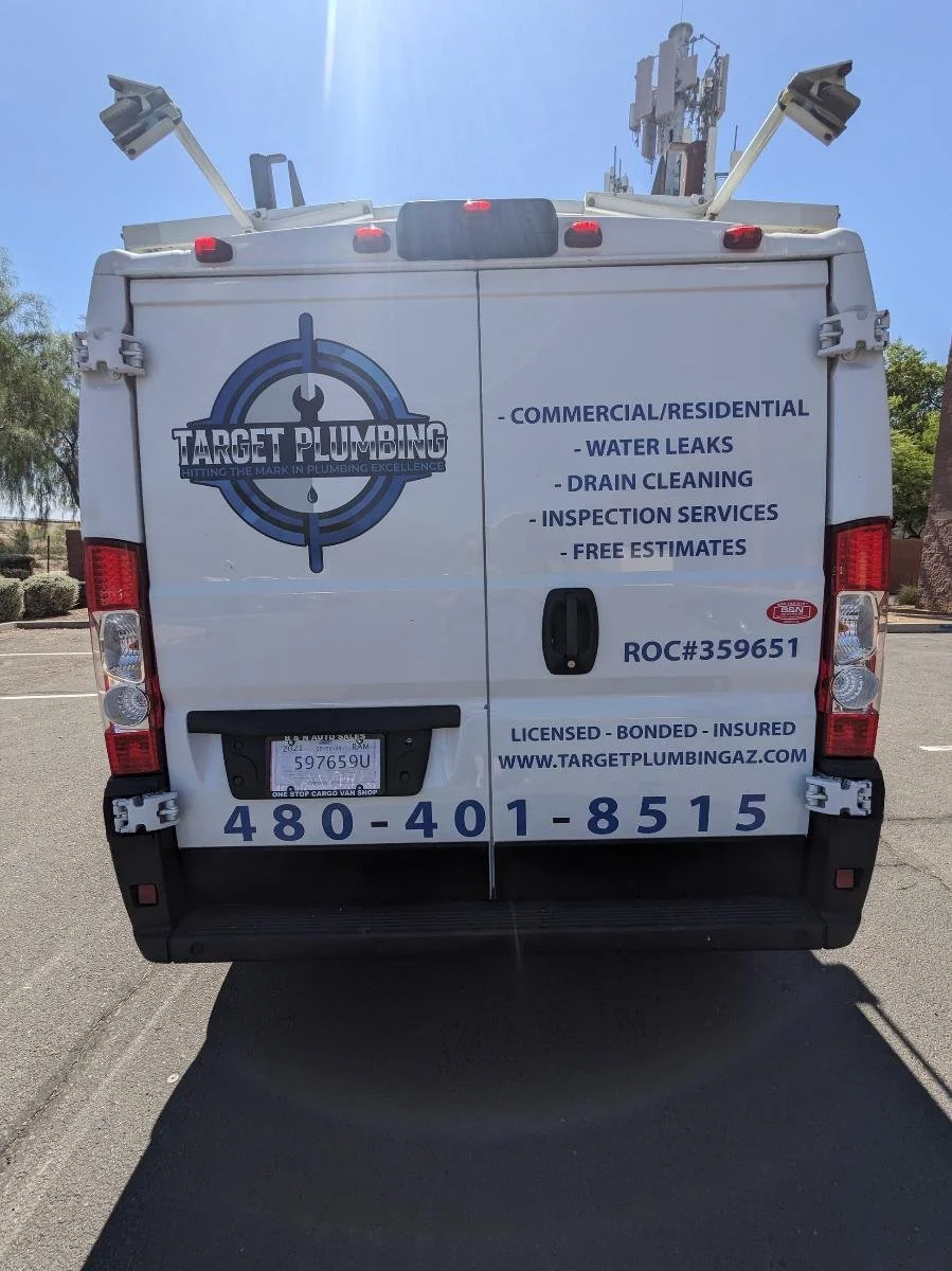 Back of a white plumbing service van with company information and service offerings, including leak repairs and drain cleaning.