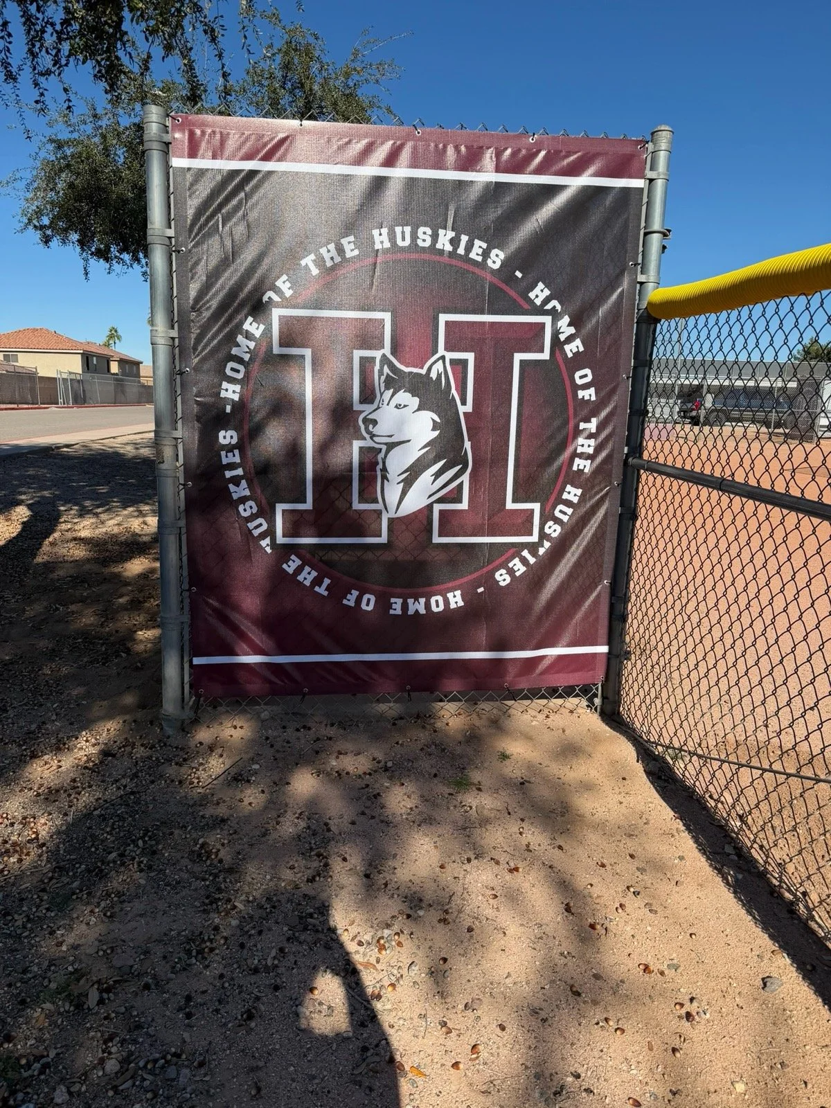 A maroon and black sports banner on a fence reads, "Home of the Huskies, I love the Huskies, Home of the Huskies," with a large letter 'H' and a husky dog logo in the center.
