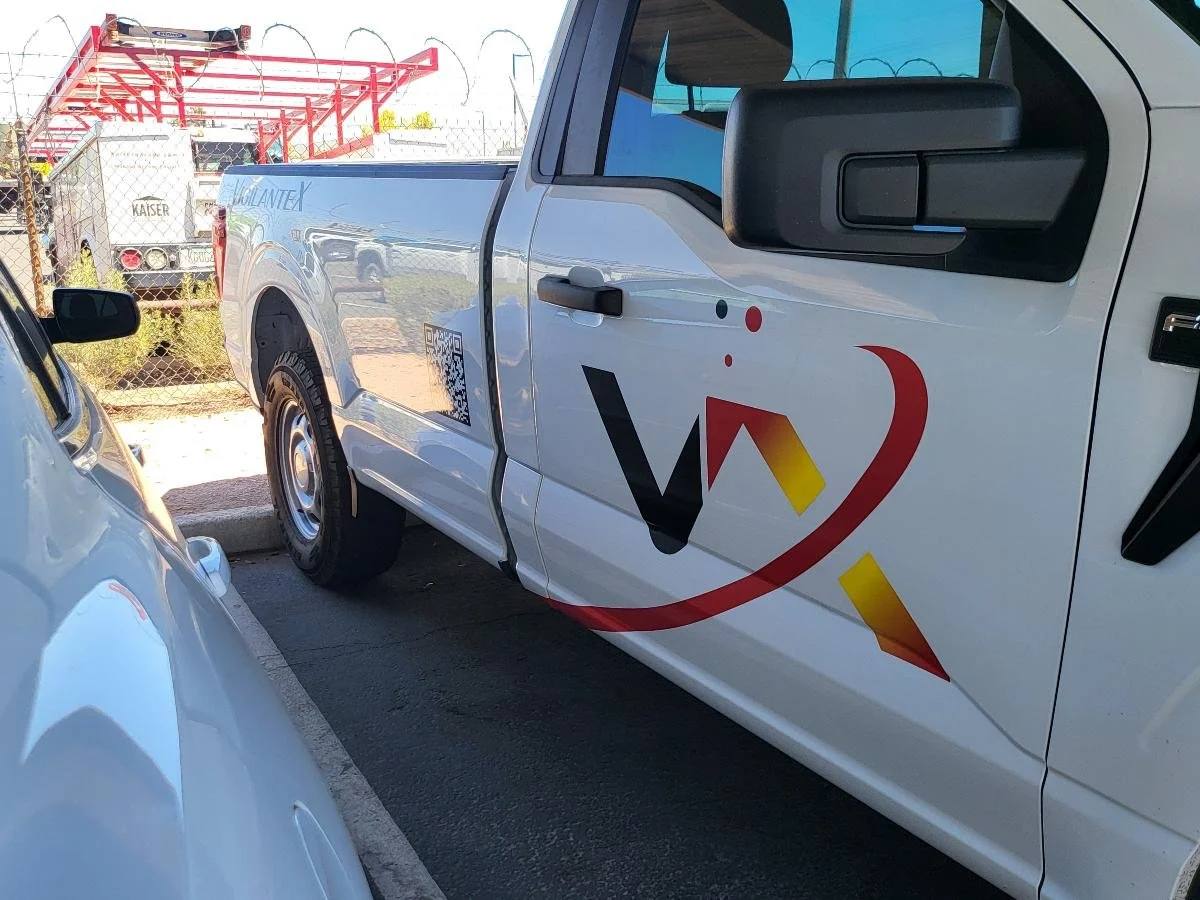 A white company truck with a logo on the door and a QR code, parked next to a white car in a parking lot.