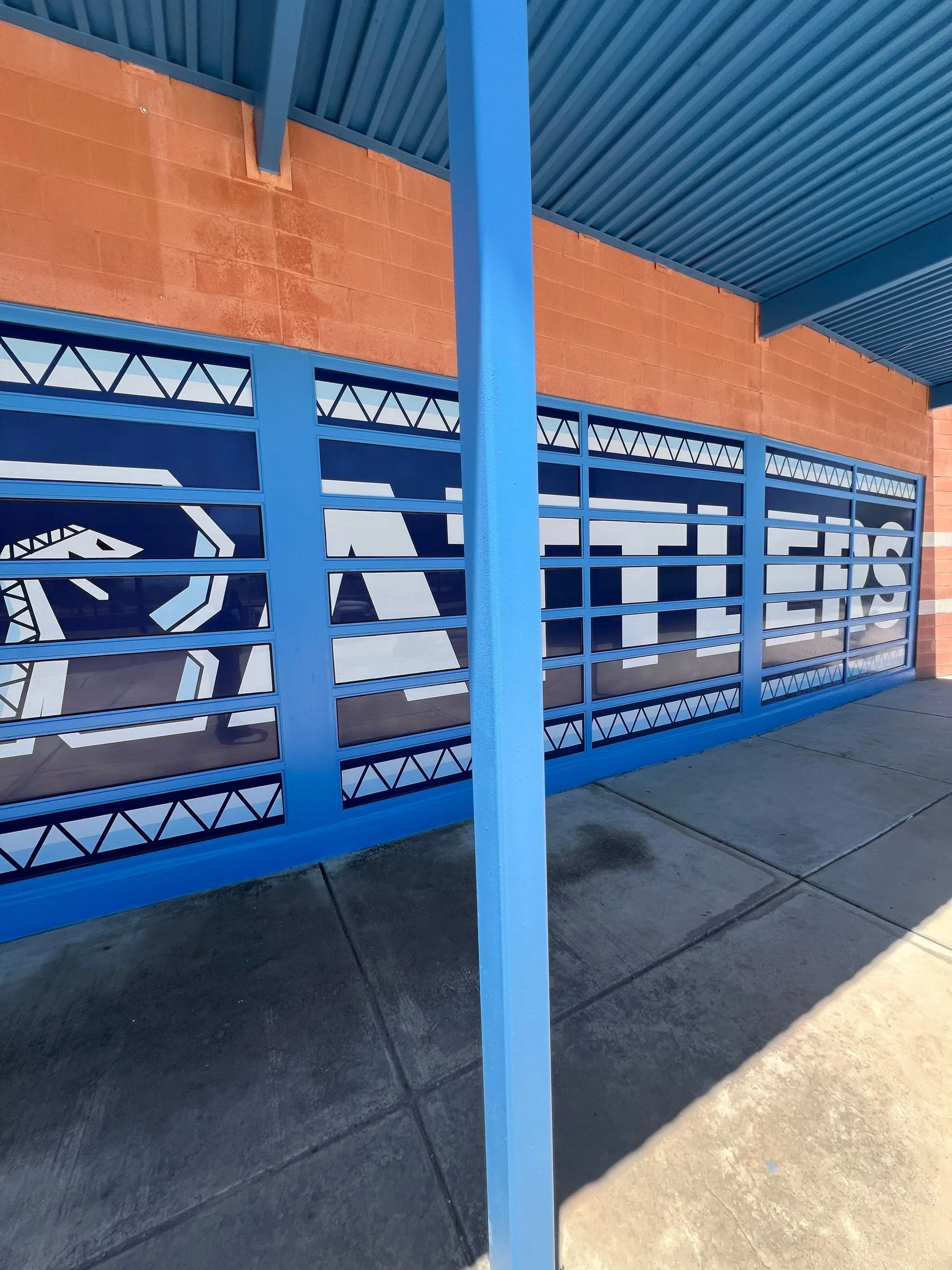 Blue metal fence with a sign that says 'ATTIC' in white and black lettering, in front of a brick building with a covered sidewalk.