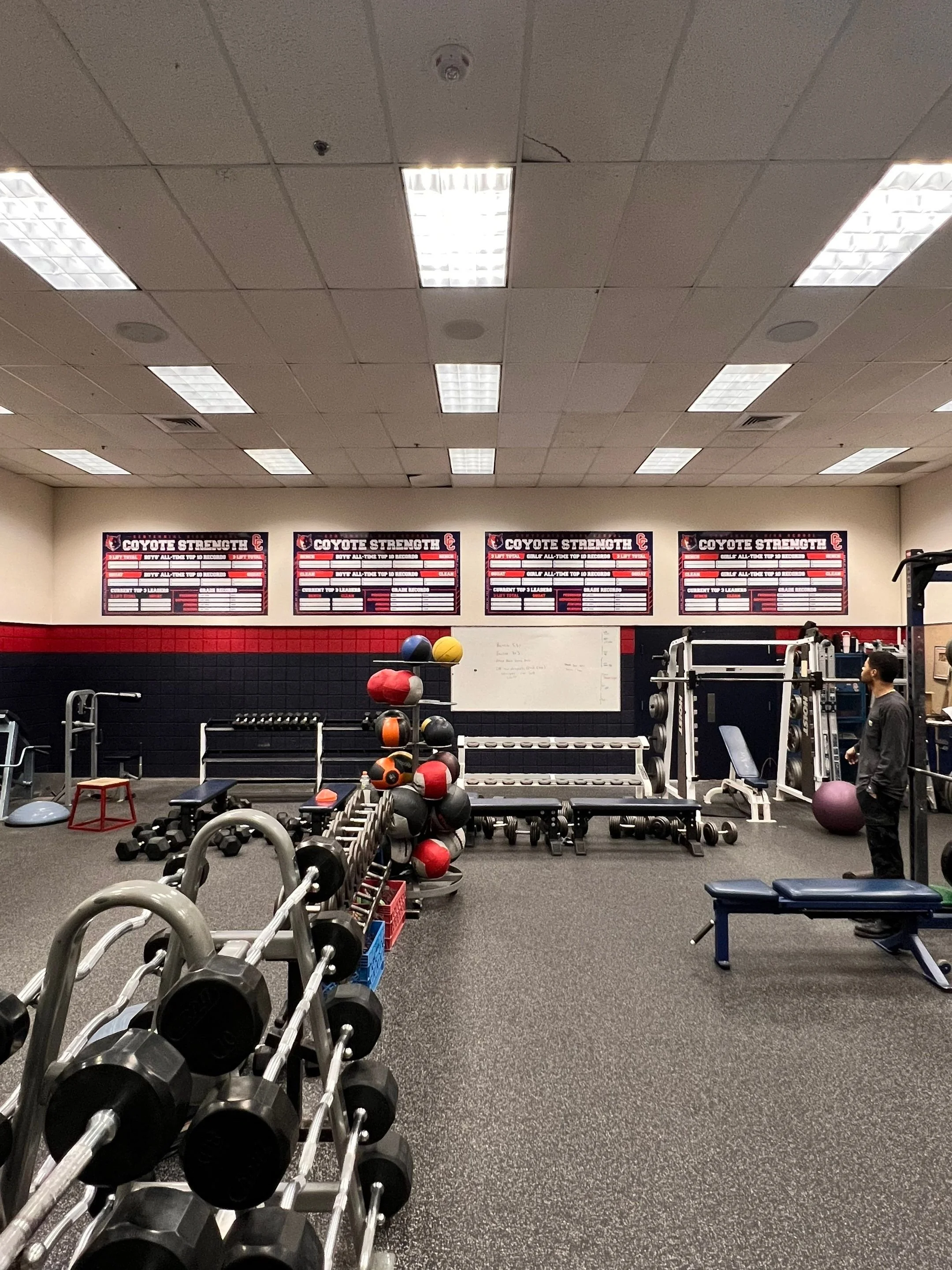 Interior of a gym with weightlifting equipment, medicine balls, and motivational posters on the wall.