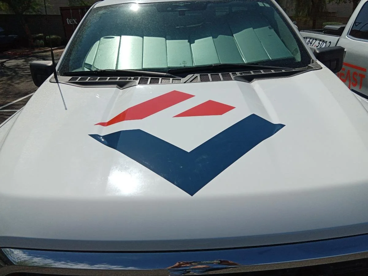 Front view of a white vehicle with a red and blue logo on the hood, parked outdoors during daytime.