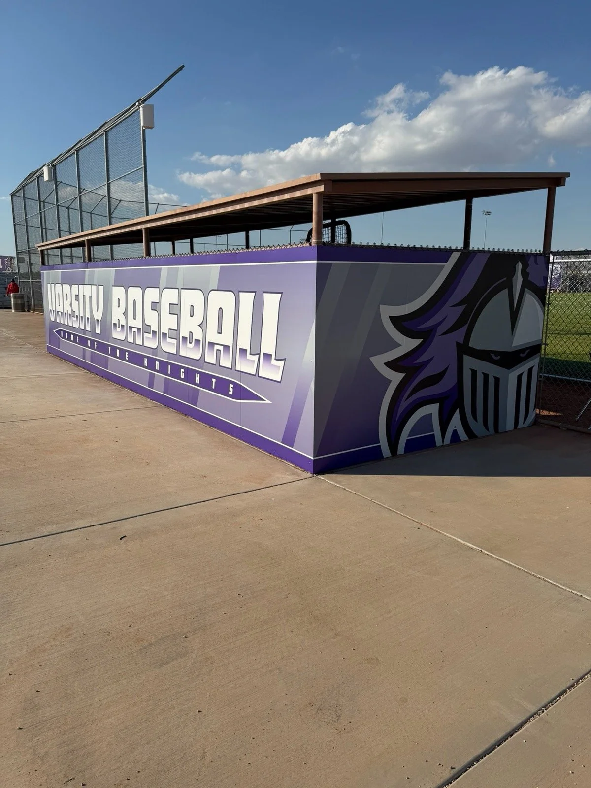 A purple and gray sign on a sports field with the words "WORCESTY BASEBALL" and a knight's helmet logo.