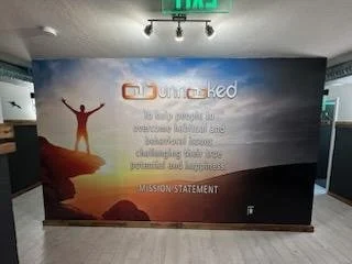 A large wall display showing the word 'Uncaged' with a person with arms raised standing on a rock at sunrise or sunset with a quote about empowering the next generation of resilient, connected, and courageous LGBTQ+ youth. The bottom has the phrase '