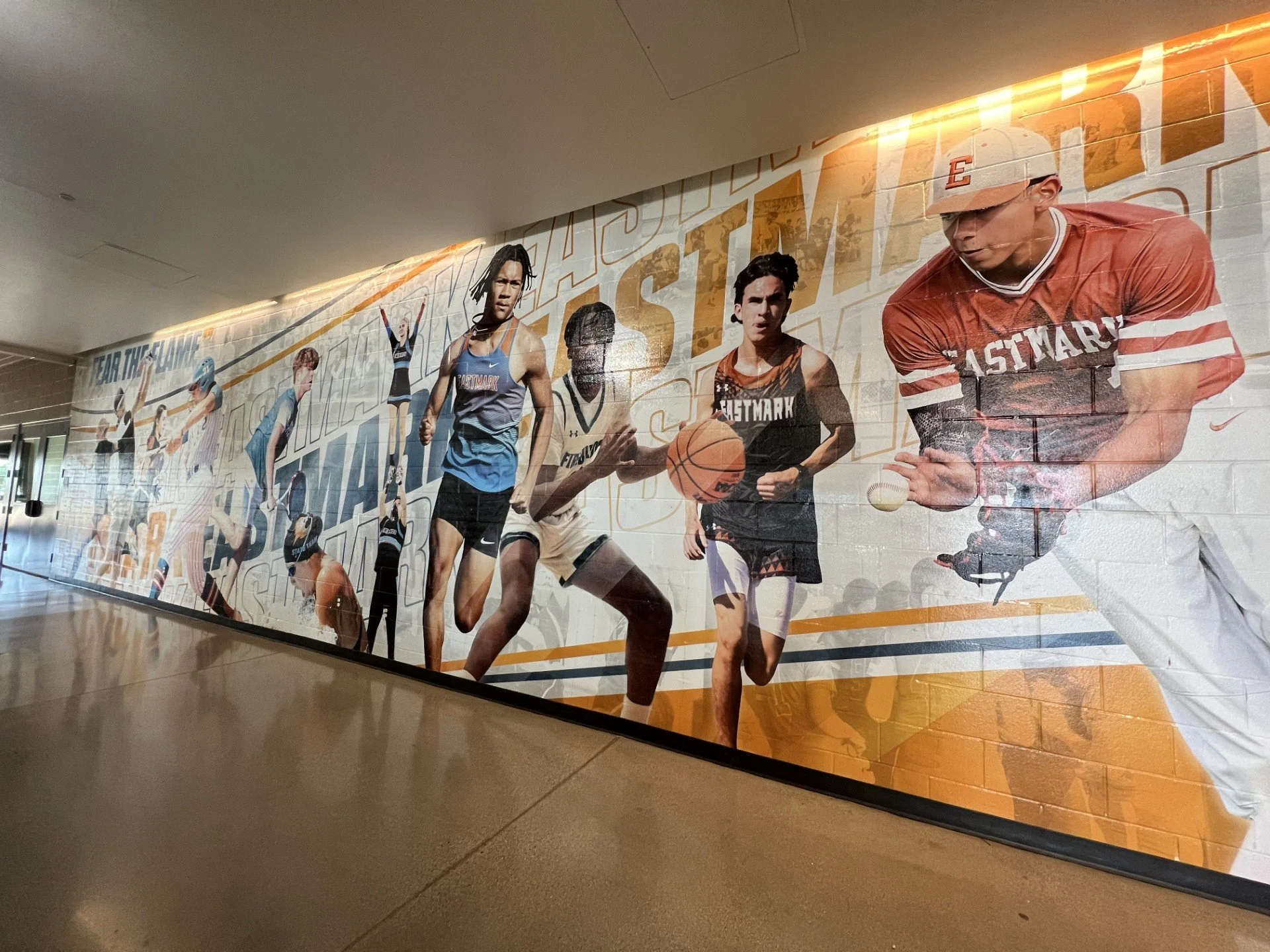 Large wall poster featuring athletes participating in various sports including running, basketball, and football, with the word 'STAY' partially visible at the top.