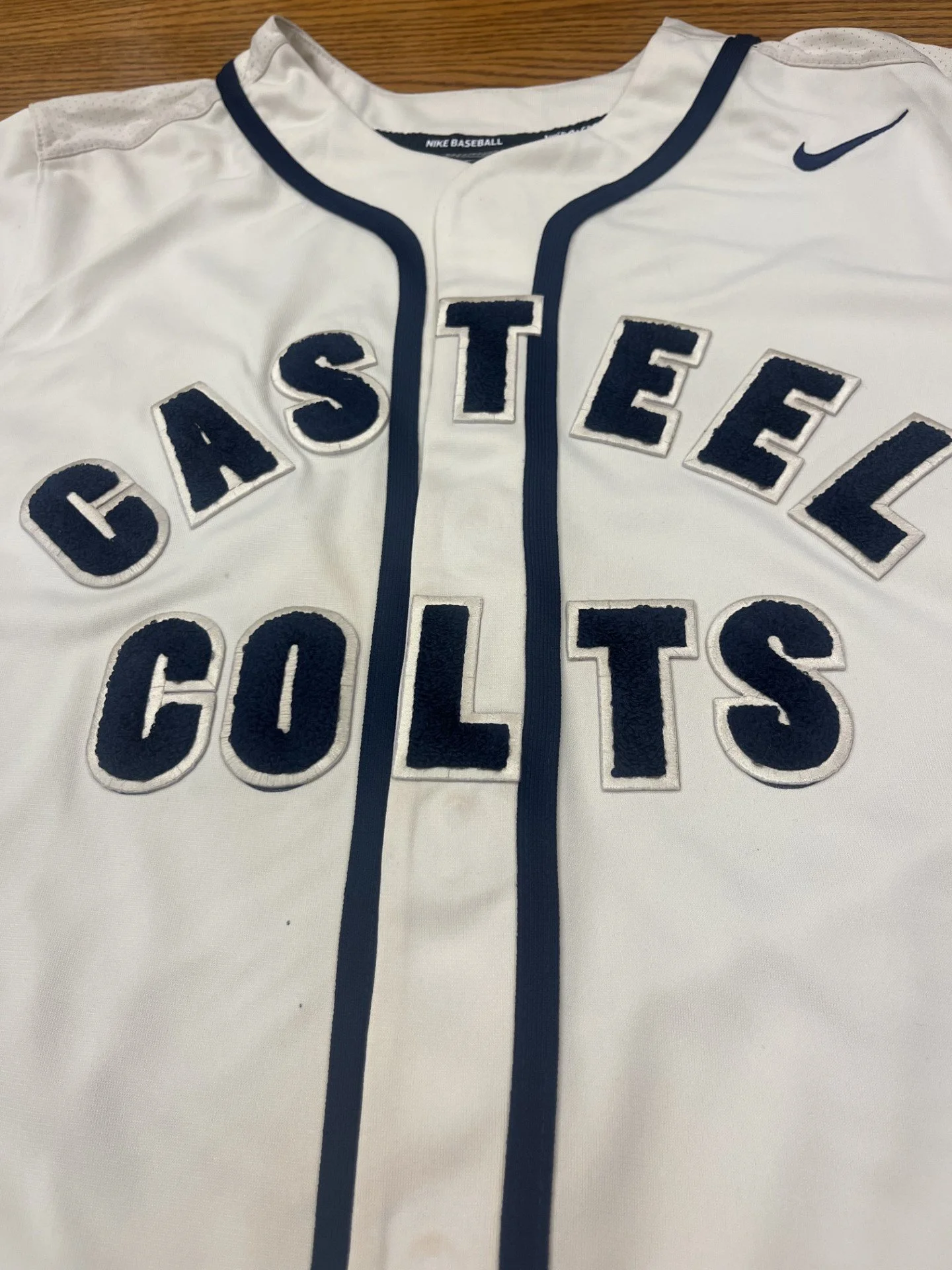 A white Nike baseball jersey with navy blue accents and large embroidered letters reading "CASTLE COLLINS".