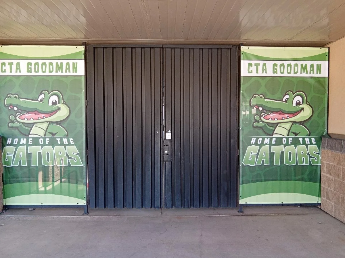 School entrance with two large banners featuring a cartoon alligator and the text "CTA GOODMAN HOME OF THE GATORS".