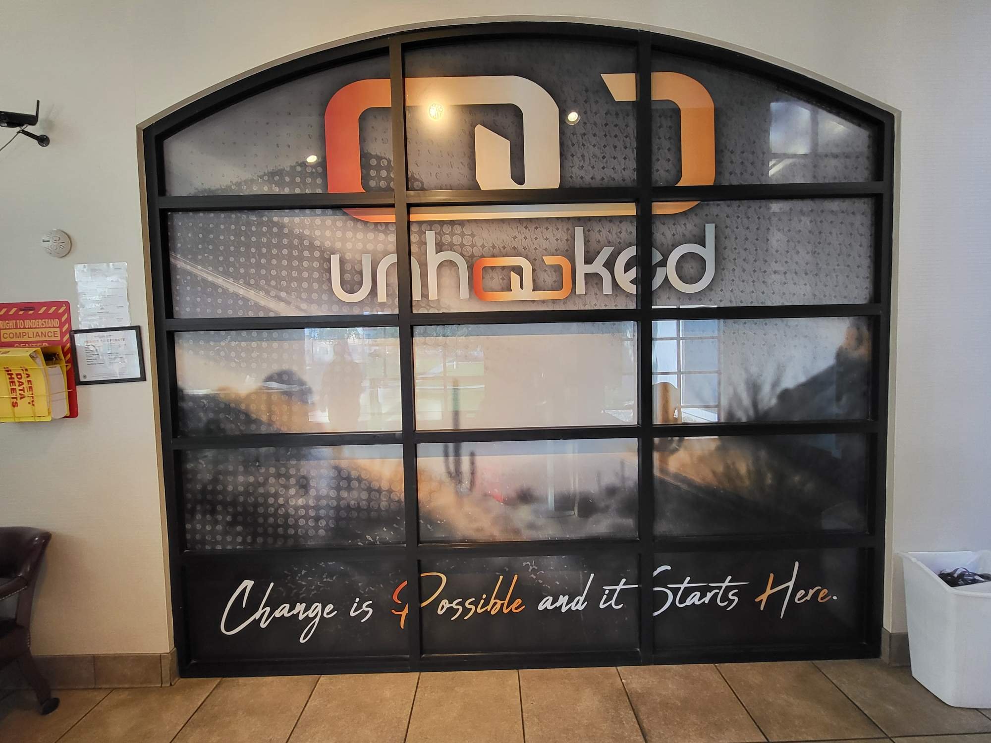 A decorative wall with a quote that says, 'Change is possible and it starts here,' written in white and orange cursive text. The wall has a black grid frame with glass panels and shows reflections of lights and surroundings.