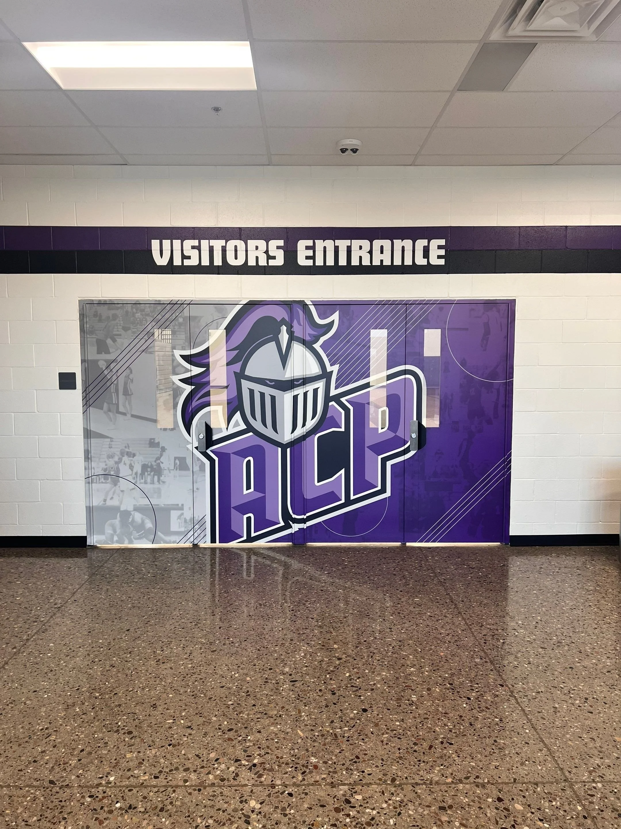 A hallway entrance with a sign above the door that says "Visitors Entrance" and large purple and white graphics featuring a knight's helmet and the letters "HOP".