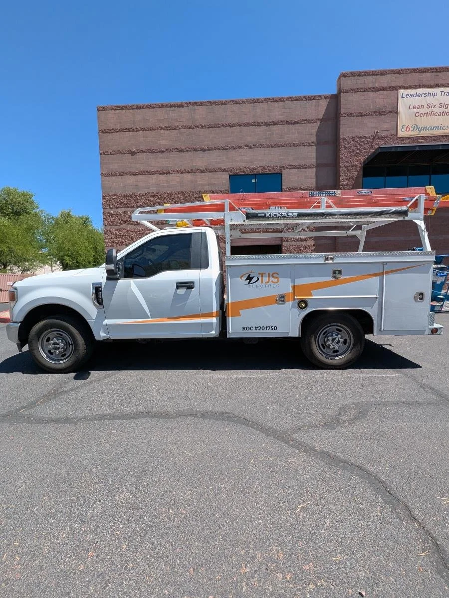 White utility truck with orange and black logo, parked in front of a brick building under a clear blue sky.