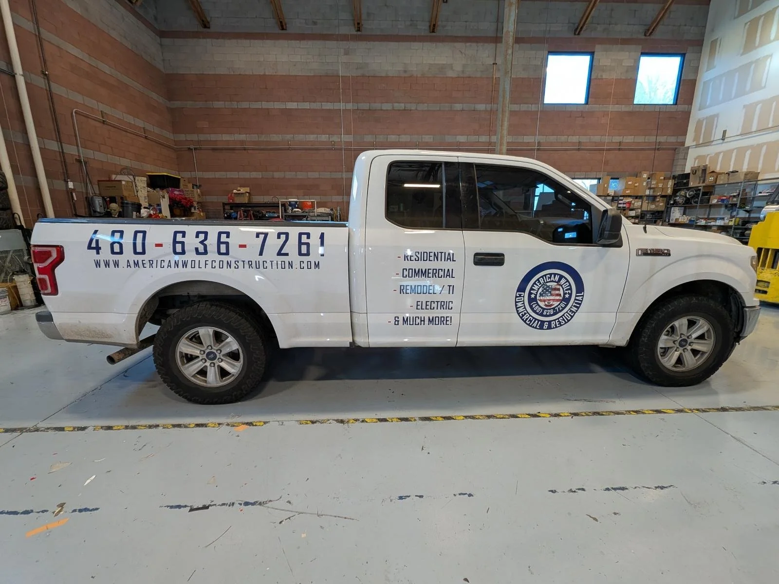 Side view of a white pickup truck with business branding for American Wolf Construction in a warehouse or garage setting.