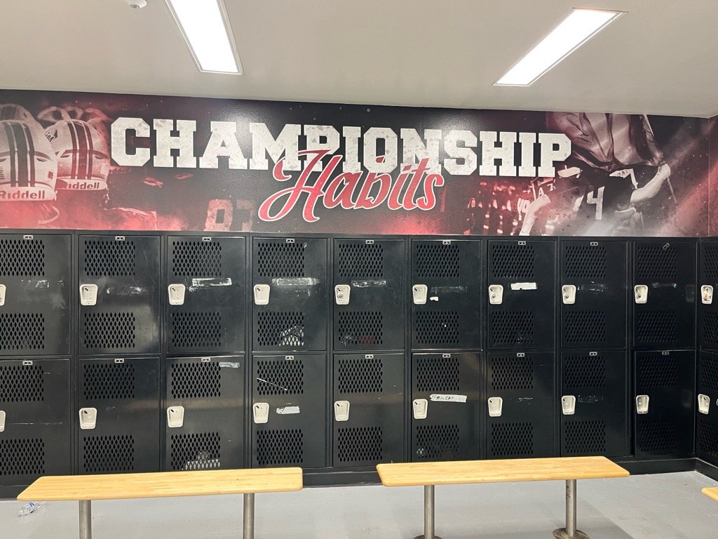 Locker room with black lockers, a motivational mural reading 'Championship Habits', and wooden benches.