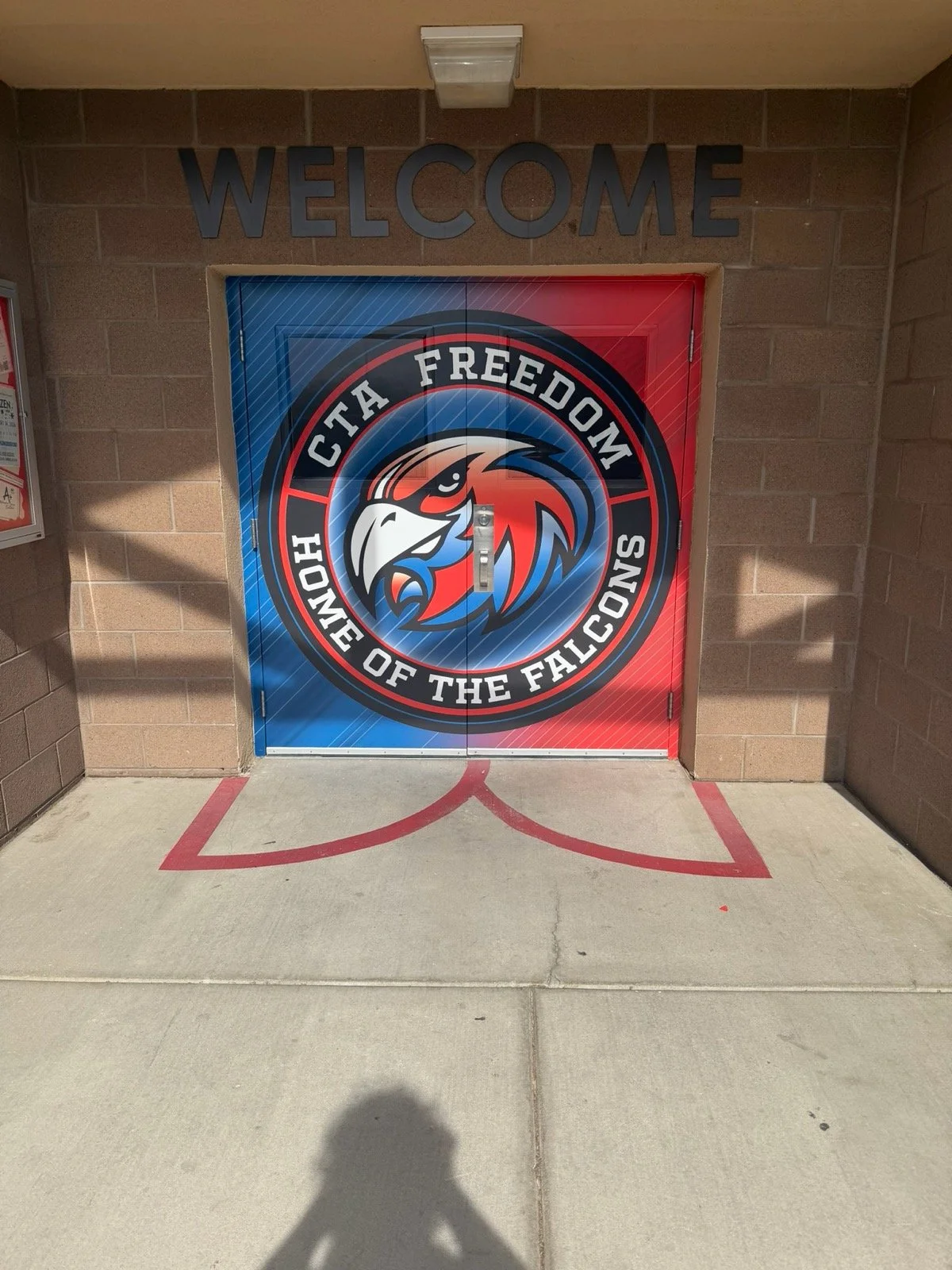 A brick wall with a colorful door featuring the logo of the CTA Freedom, a team in the League of the Falcons, with a large 'Welcome' sign above.
