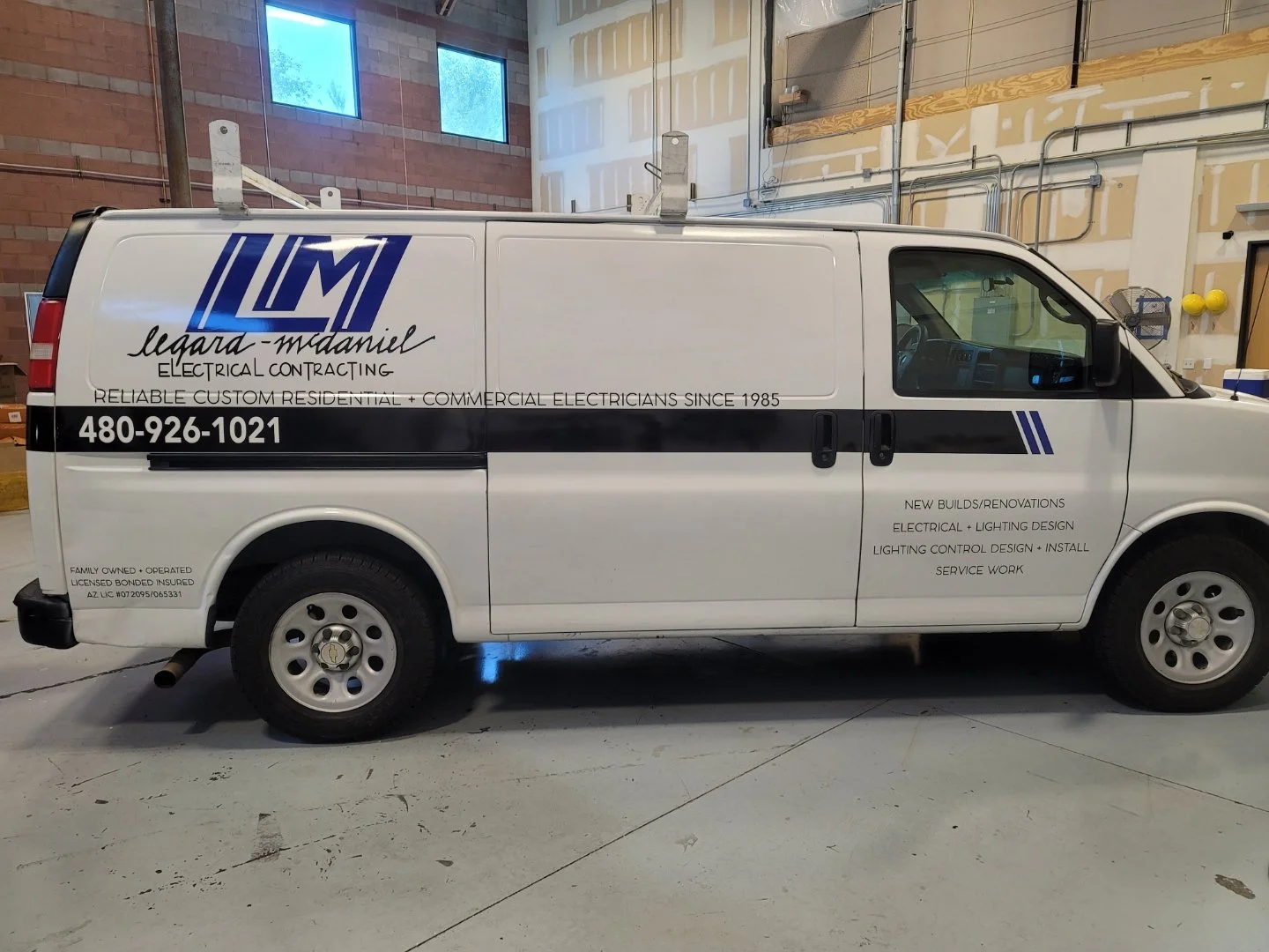 White service van parked indoors, with company logo and contact information on the side, advertising electrical contracting services.